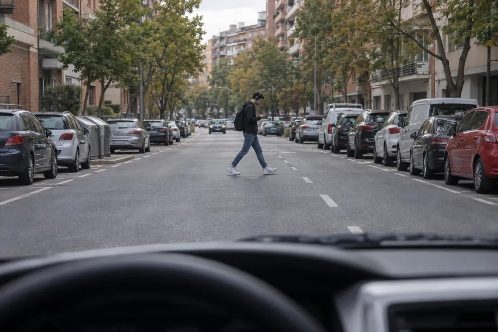 Peatón mirando el móvil que cruza por mitad de la calzada, lejos de cualquier paso.