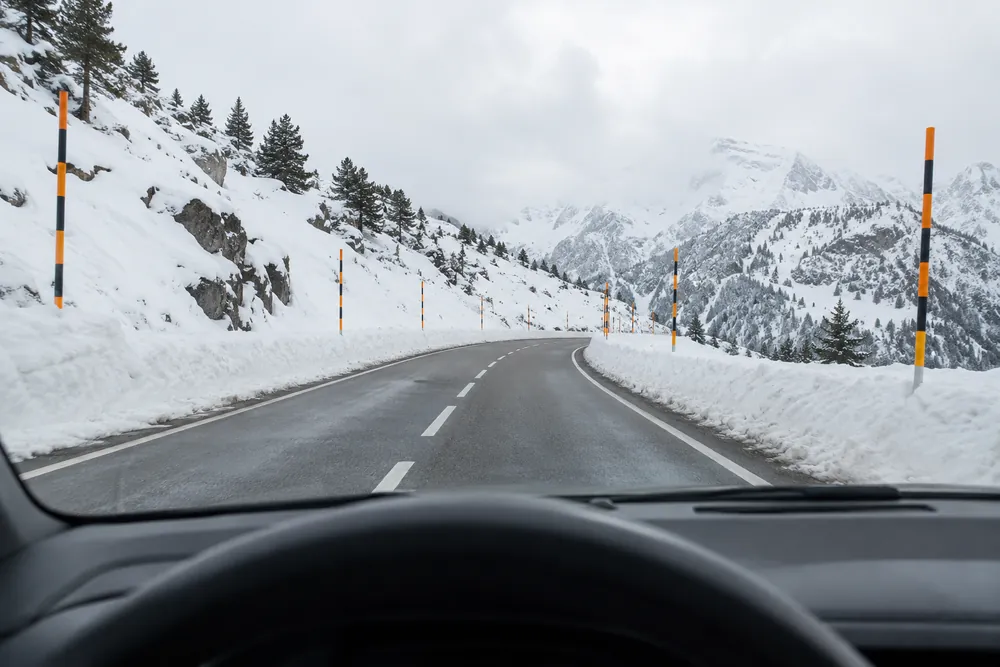 Puerto de montaña nevado con postes altos que marcan el borde de la calzada.