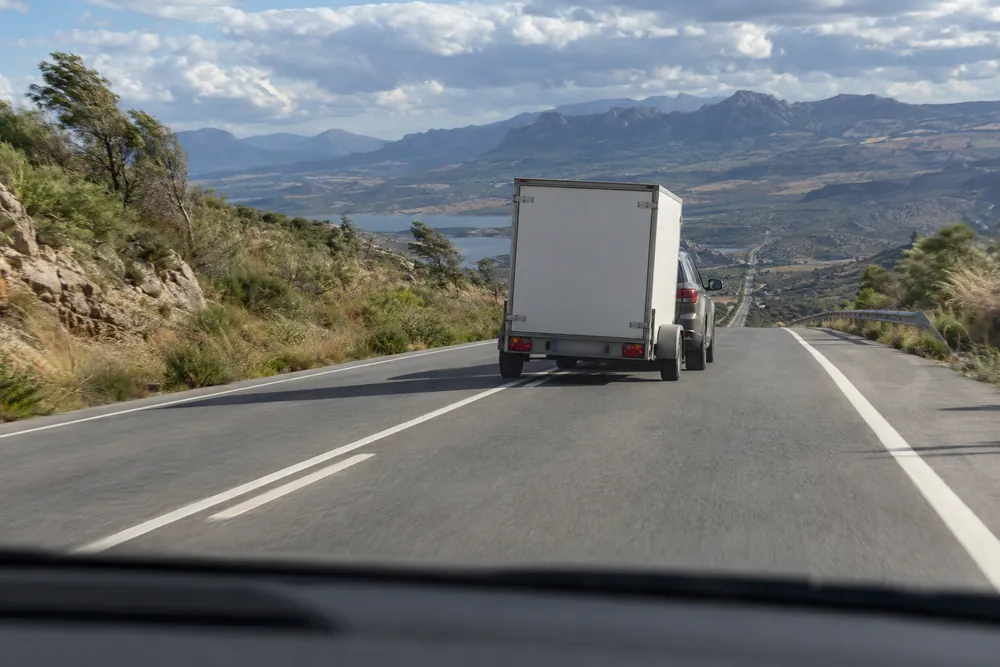 Turismo con remolque en una bajada, con el remolque desplazado hacia un lado, visto desde detrás.
