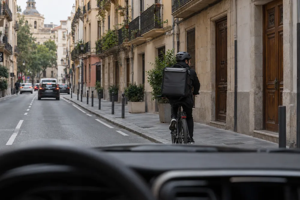Repartidor en bicicleta con una gran mochila de reparto circulando por la ciudad.