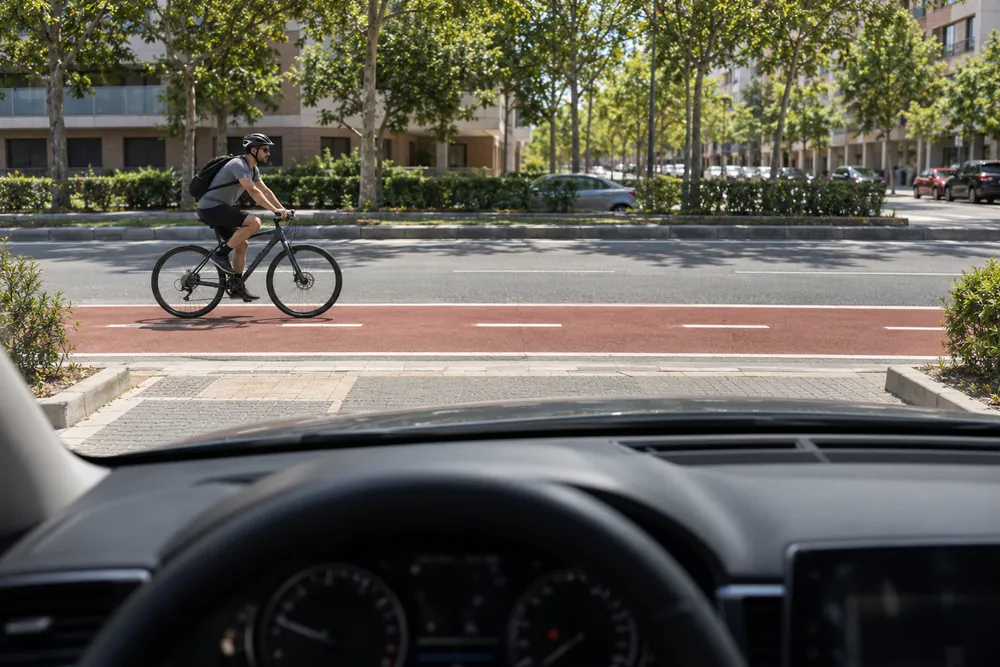Turismo saliendo de un aparcamiento a la calzada mientras por el carril bici contiguo llega una bicicleta.