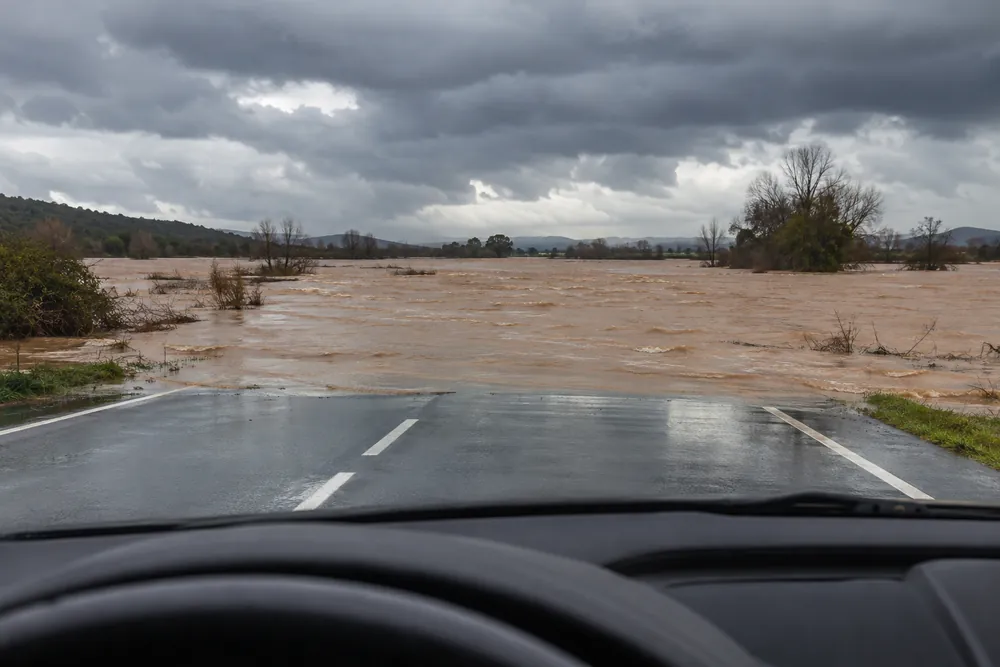 Tramo de carretera cubierto por agua de una crecida, visto desde el coche que se acerca.